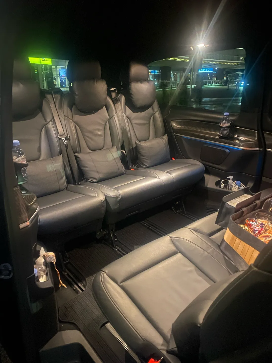 Van Mercedes Classe V de nuit, porte ouverte — configuration salon en cuir noir avec le panier d’attentions posé sur un siège