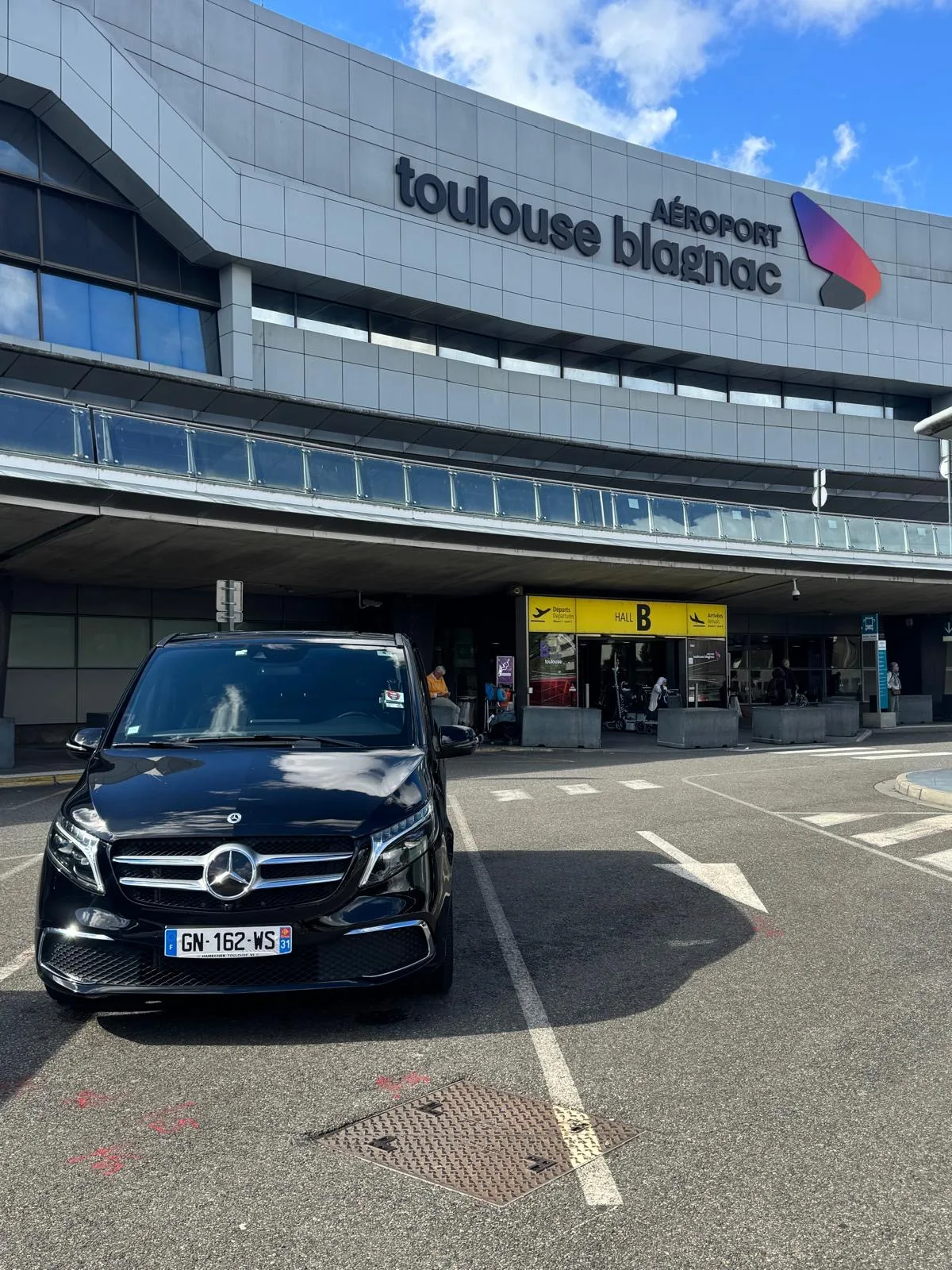 Navette privée à Toulouse : van Mercedes Classe V noir devant l’entrée du hall B de l’aéroport Toulouse-Blagnac, départs et arrivées