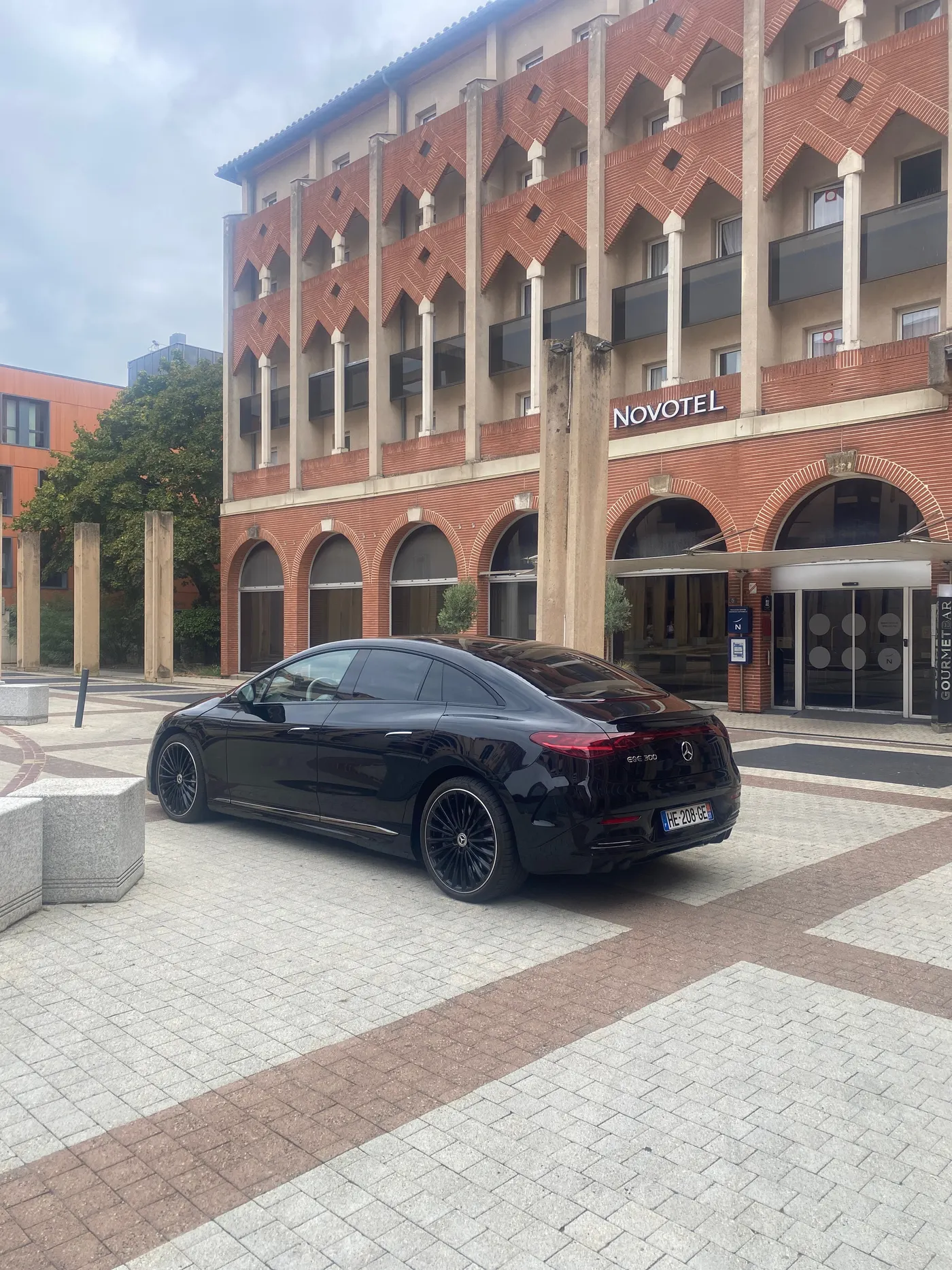 Navette privée Toulouse : berline Mercedes EQE noire devant la façade en brique d’un hôtel Novotel à Toulouse, prise en charge d’un client